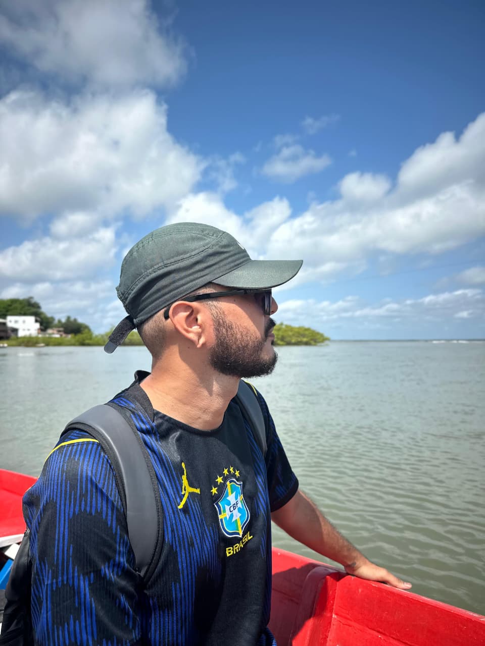 Caio Maia Almeida olhando o horizonte de um barco, de boné e óculos escuros